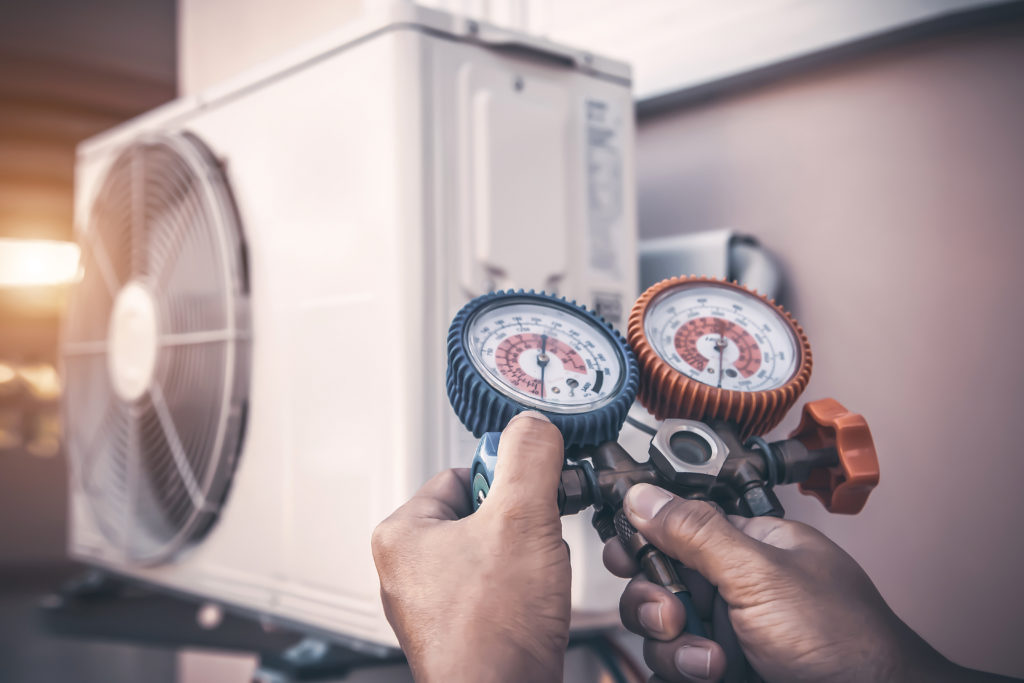 Air repair mechanic using measuring pressure gauge equipment for filling home air conditioner after cleaners and checking maintenance outdoor air compressor unit.
